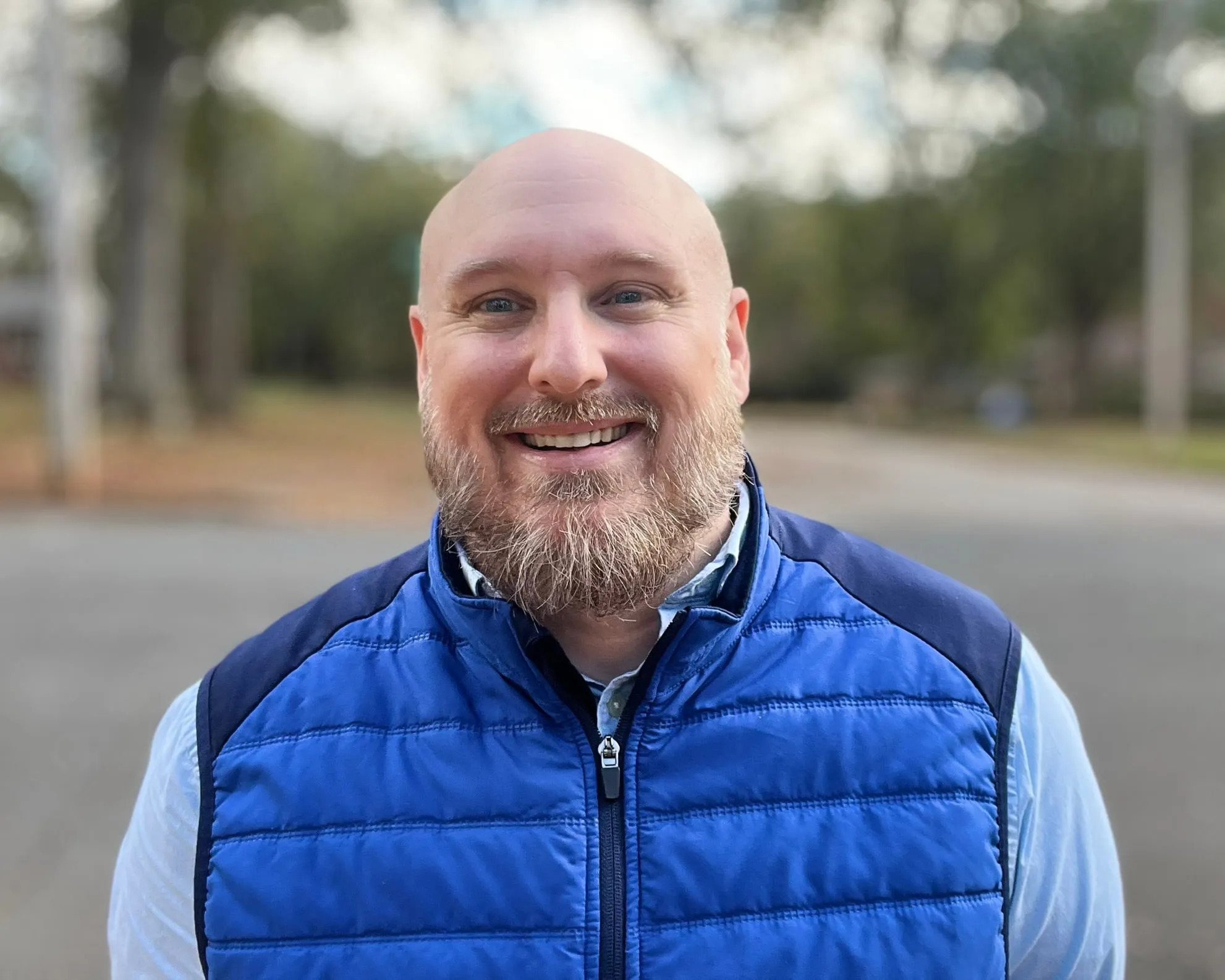 David Hennes smiling outdoors in a blue vest
