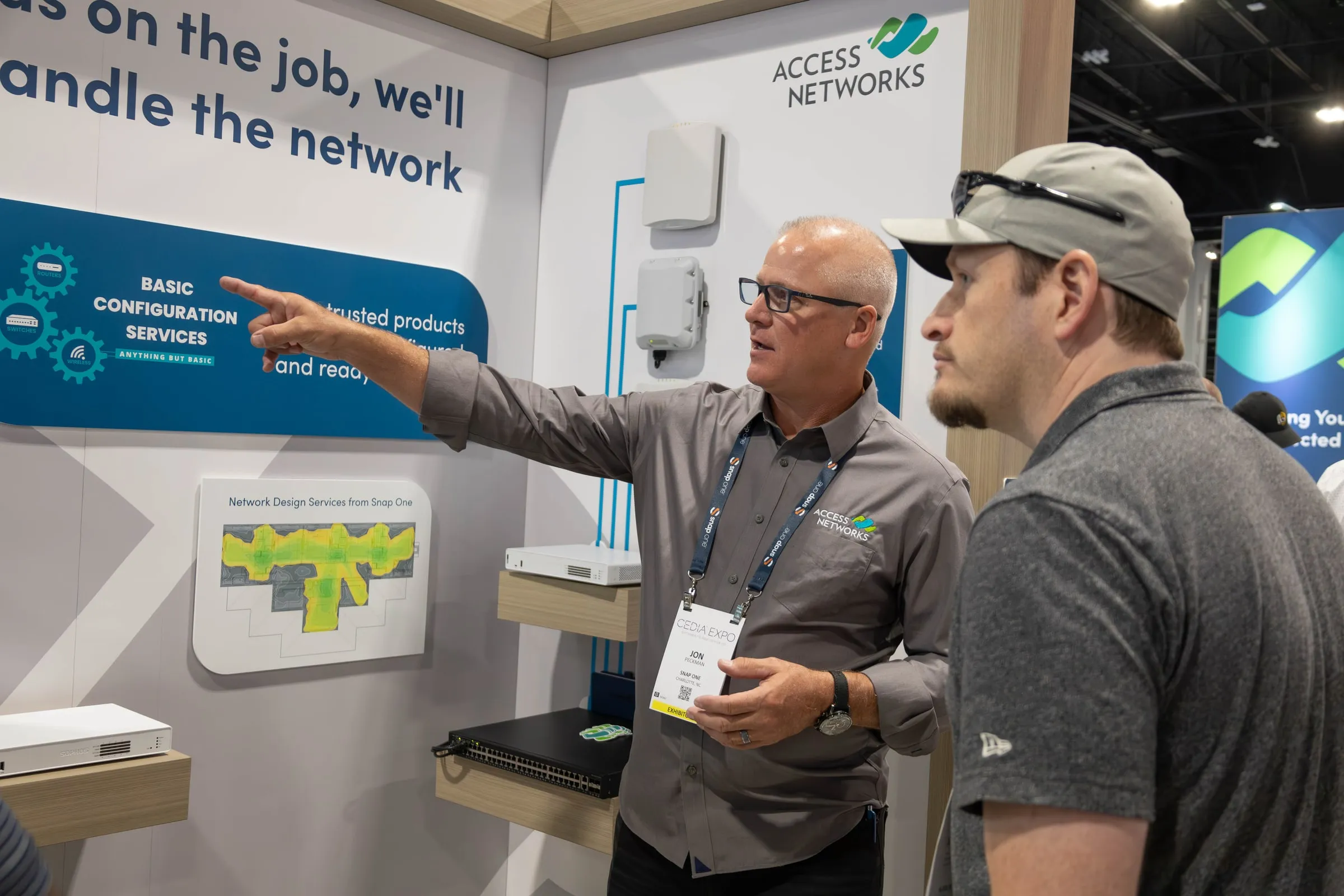Booth staff member explaining an Access Networks display to a visitor