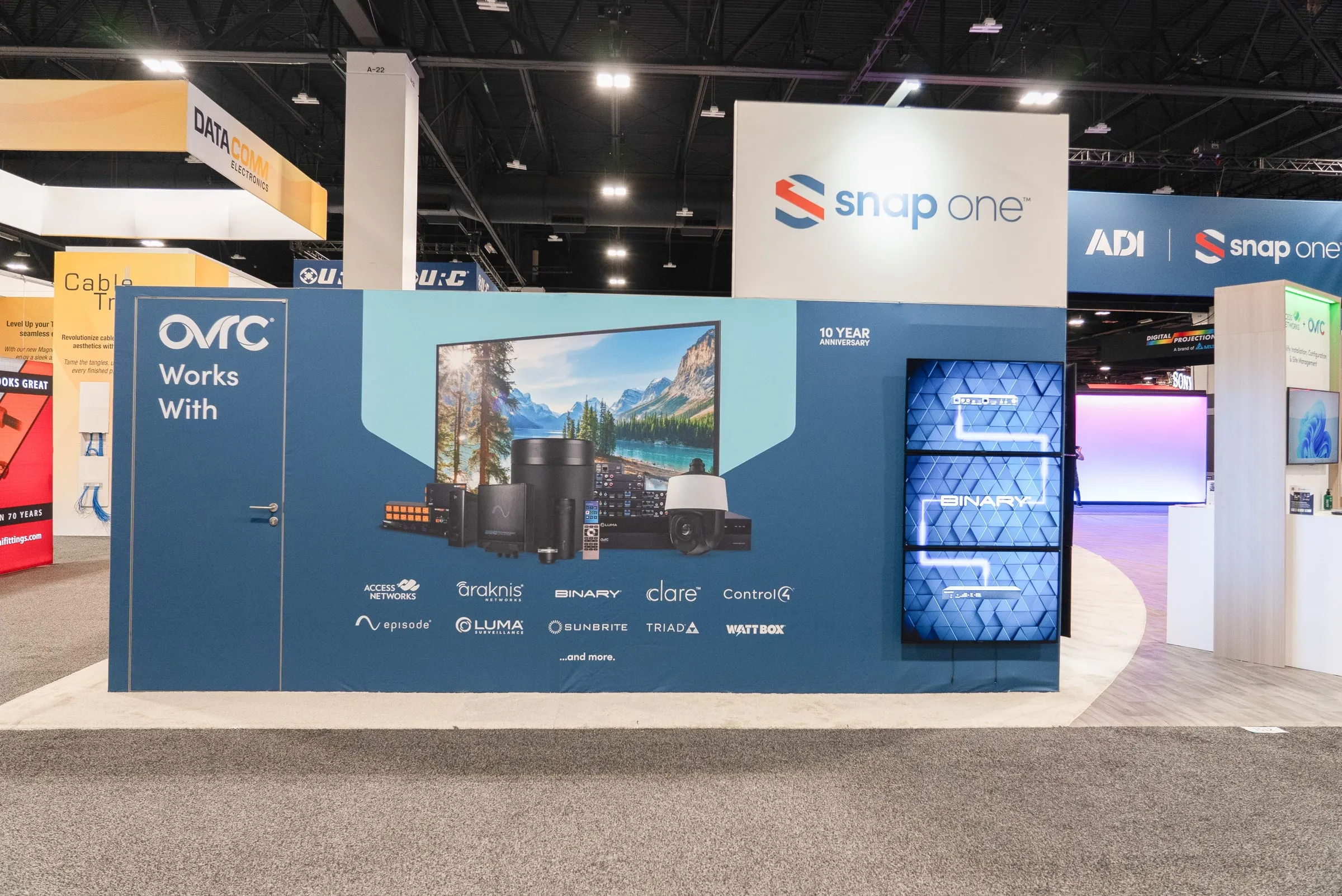 OvrC "Works With" wall with a large screen and partner logos