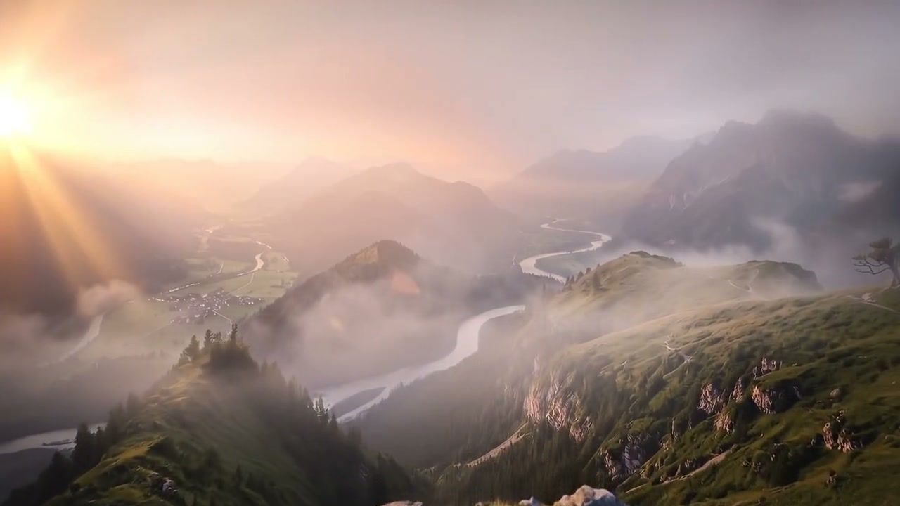 Misty mountain valley at sunrise with a river winding below