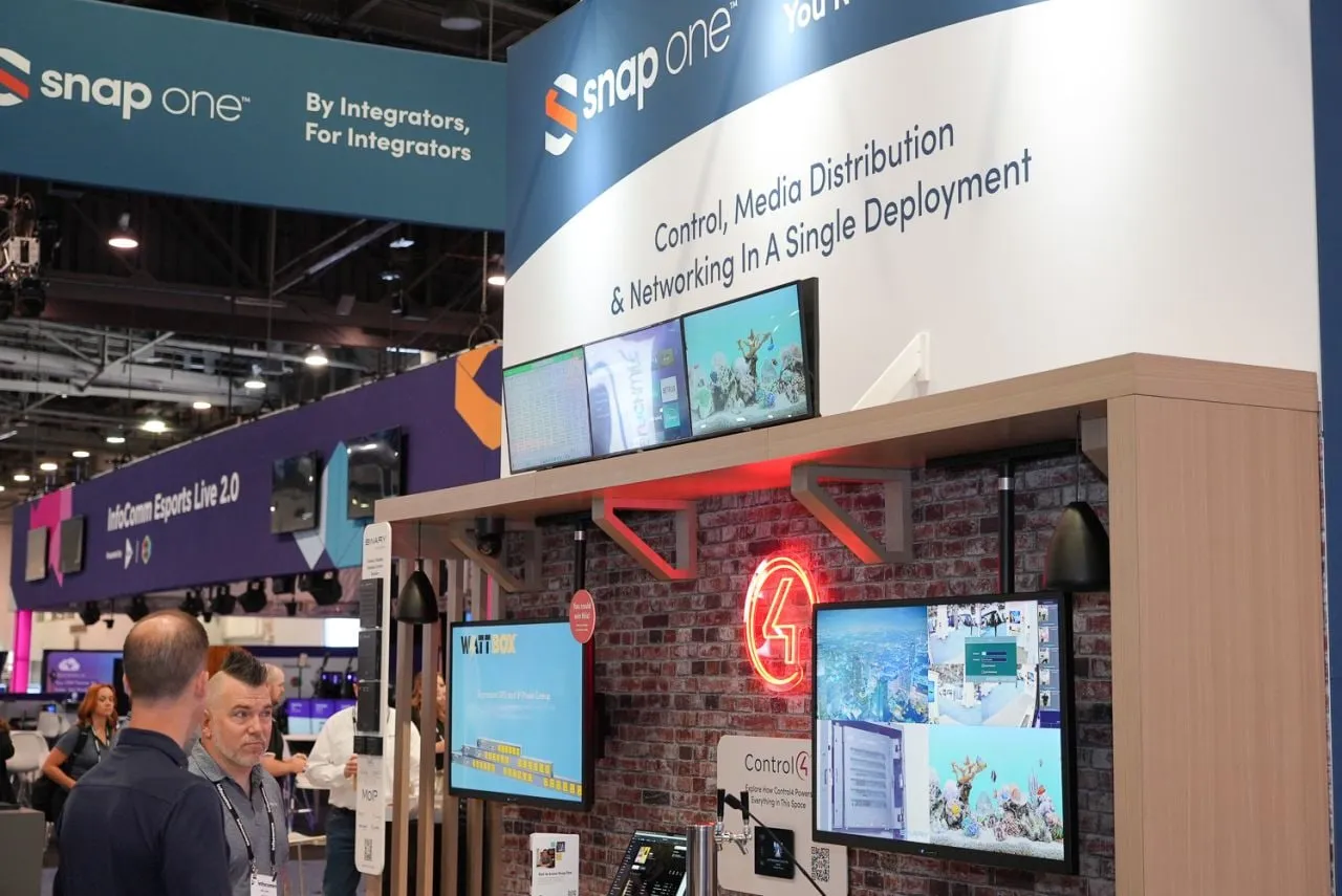 Snap One InfoComm 2024 booth: "Control, Media Distribution and Networking in a Single Deployment" with a brick wall and TVs