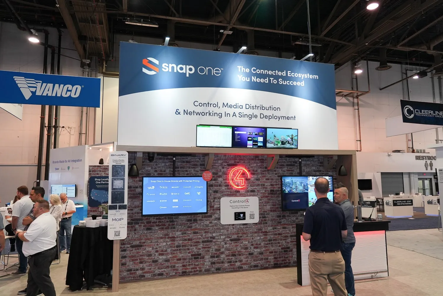 Brick wall demo area with TVs and a Snap One header