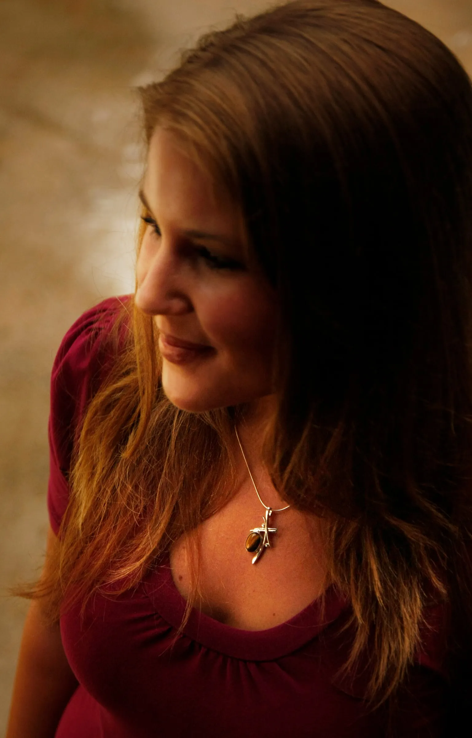 Model with long hair wearing a pendant necklace, warm indoor light