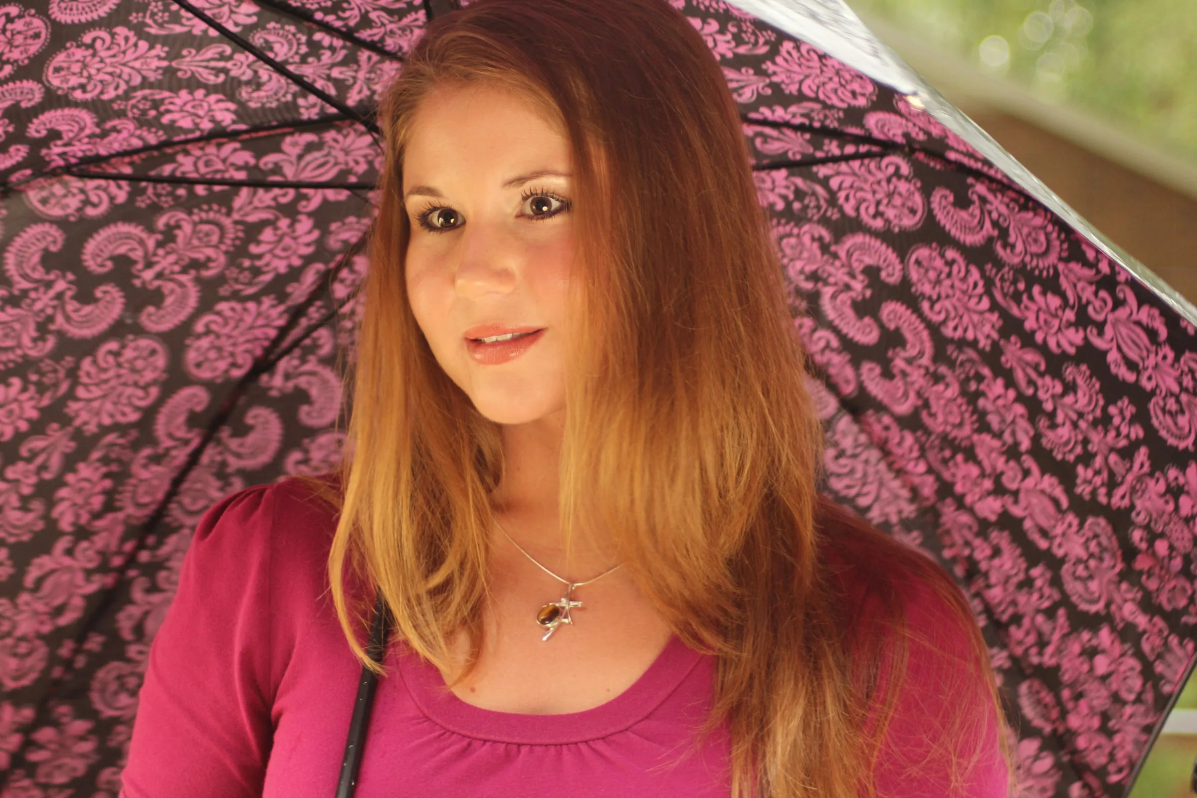 Model under a pink patterned umbrella wearing a pendant necklace