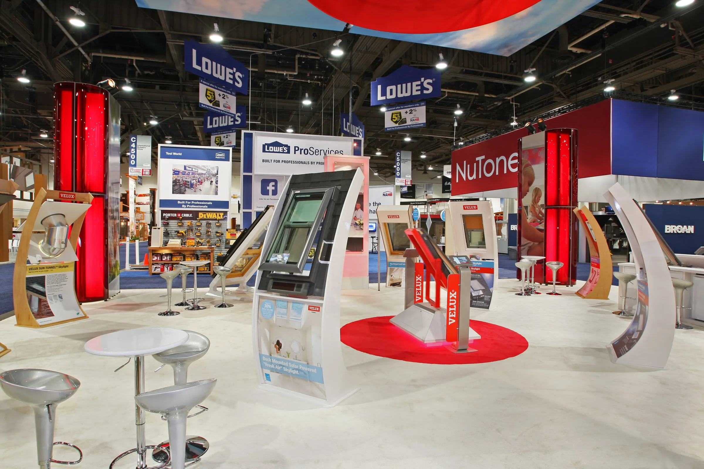 Wide view of a VELUX trade show booth with tall red VELUX towers and an overhead sky banner (3 of 3)